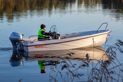Poika ajaa pienellä moottoriveneellä syksyisessä maisemassa. Edessä näkyy kaisloja.