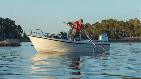 A man is lifting a fish catch into the Terhi Nordic 6020 C console boat with a landing net.